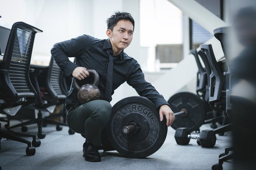 オフィスでケトルベルとバーベルのトレーニング器具を比較検討する経営者