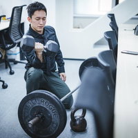 オフィスでダンベルトレーニングする男性の上腕二頭筋チェックの写真