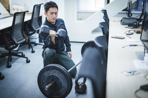 オフィスでダンベルトレーニングする男性の上腕二頭筋チェック