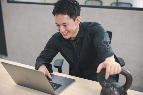 ケトルベルを持ちながらパソコンを見て笑う社長の