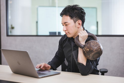 デスクワーク中にケトルベルで左腕を鍛える男性