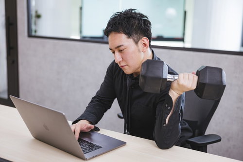 デスクワーク中にダンベルで左腕を鍛えるマッスル経営者