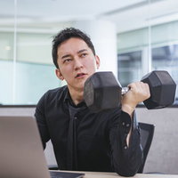 オフィスのデスクでダンベルを持ち上げた不機嫌な男性経営者の写真