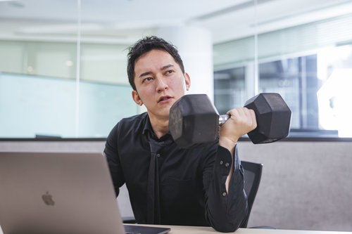 オフィスのデスクでダンベルを持ち上げた不機嫌な男性経営者