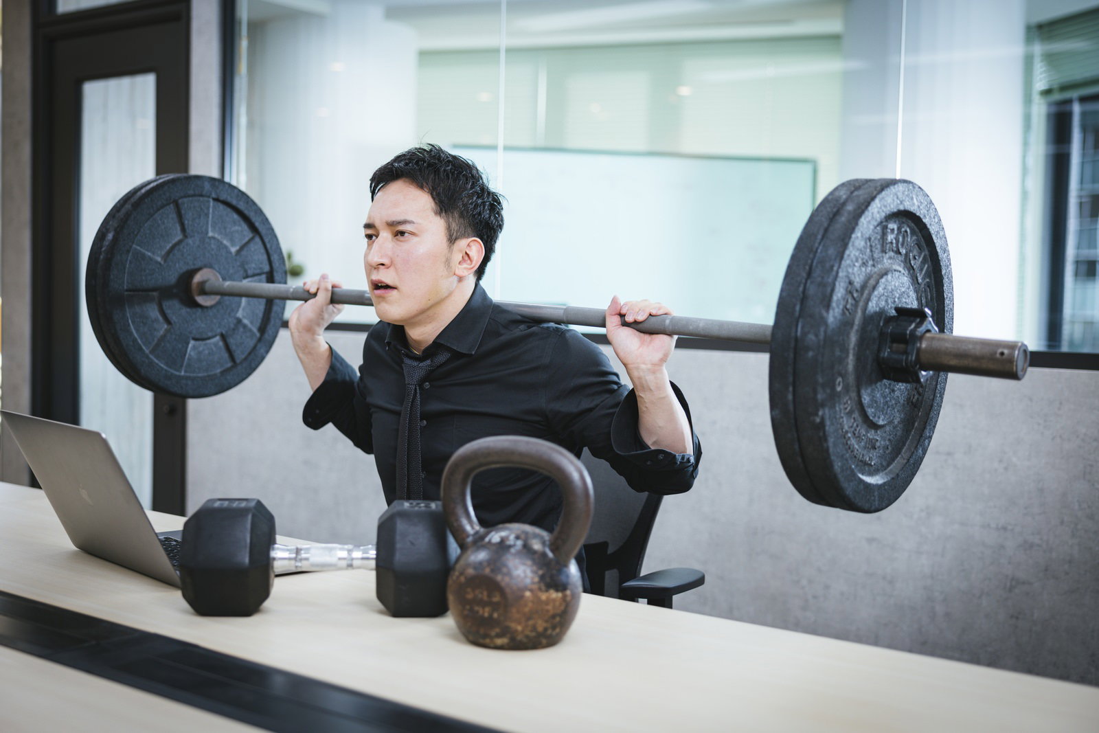 オフィスでバーベルを担いでトレーニングする男性経営者［モデル：鈴木秀］
