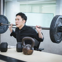 オフィスでバーベルを担いでトレーニングに気合を入れる経営者の男性の写真