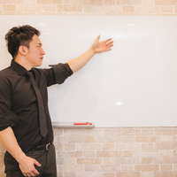 ホワイトボードに説明する経営者の左腕とジェスチャーの写真