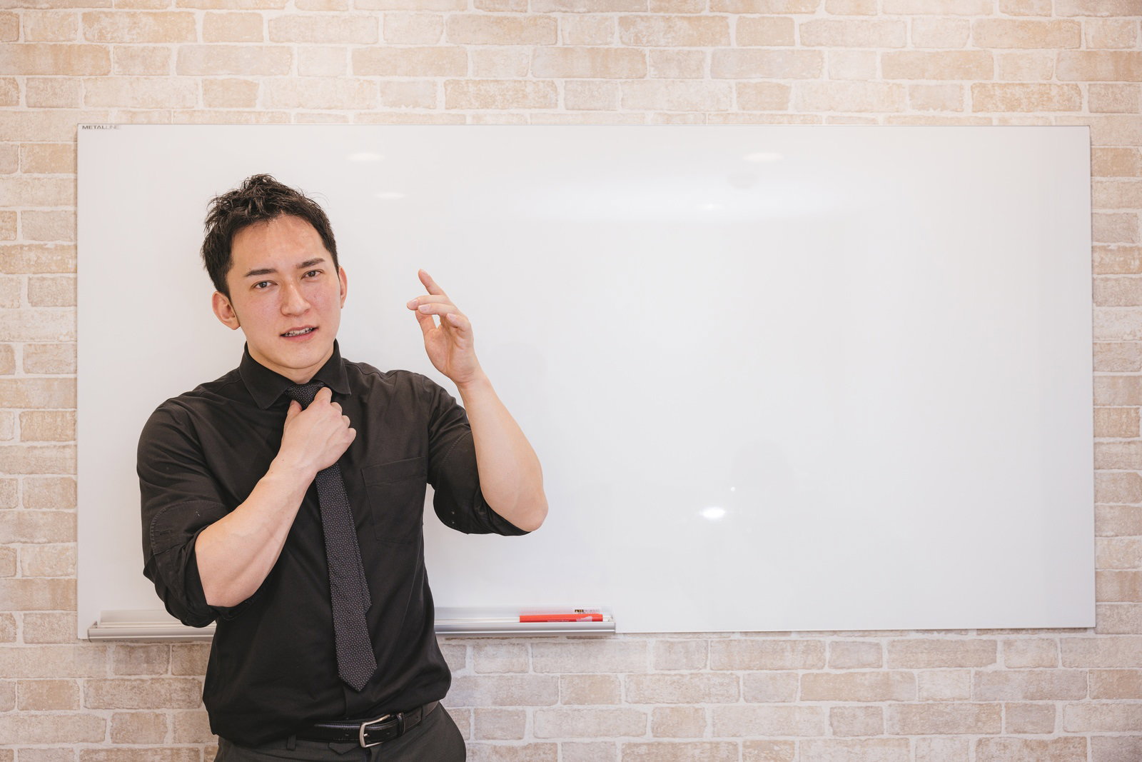 ホワイトボードの前で話す黒いシャツの男性経営者［モデル：鈴木秀］