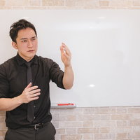 ホワイトボードの前で身振り手振りを交えてプレゼンする若い経営者の男性の写真