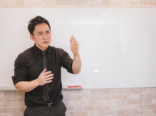 ホワイトボードの前で身振り手振りを交えてプレゼンする若い経営者の男性