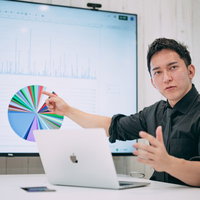 モニターに出力された円グラフを見てディスカッションする経営者の男性の写真