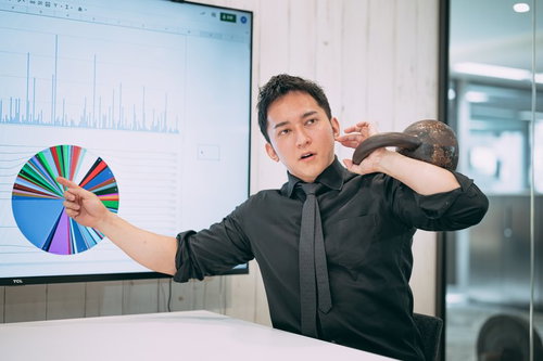 ケトルベルを持ち上げながらグラフを指すオフィスでのプレゼン