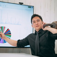 ケトルベルを肩に担ぎながらプレゼンするビジネスマンの写真