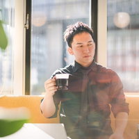 高層ビルが見えるカフェでコーヒーブレイクするマッスル経営者の写真