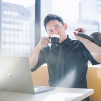 休憩中にコーヒーとケトルベルで気分転換する男性の写真