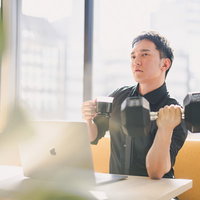 ダンベルで鍛えながら飲むプロテインで一息つく男性の写真