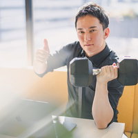 デスクワーク中でも余裕の表情でダンベル筋トレする男性社長の写真