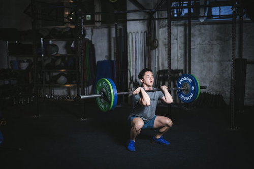 スクワットクリーンで緑と青のバーベルを持ち上げる男性