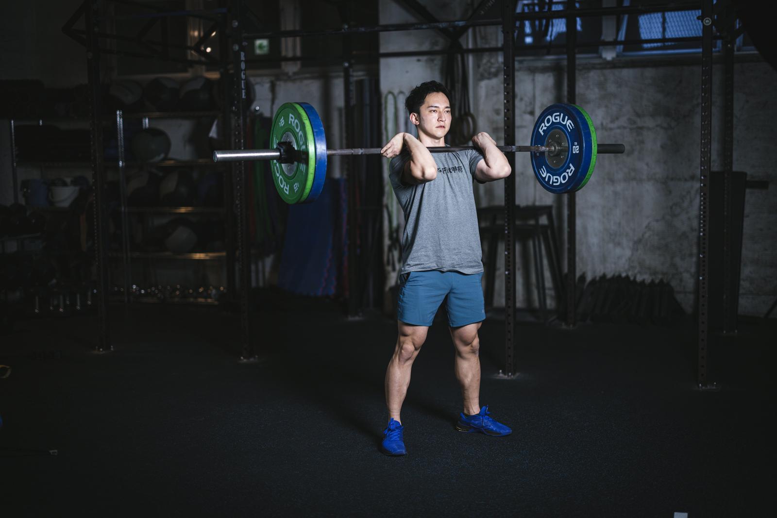 ジムでバーベルを担ぐ男性トレーニーの集中した表情［モデル：鈴木秀］
