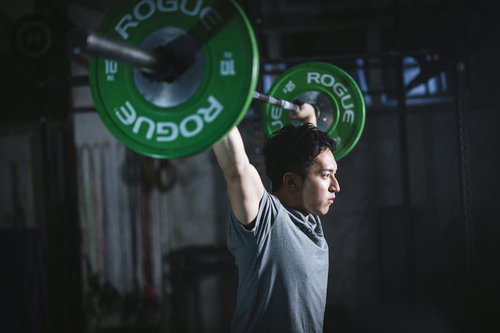 緑のバーベルを頭上に持ち上げるアスリート