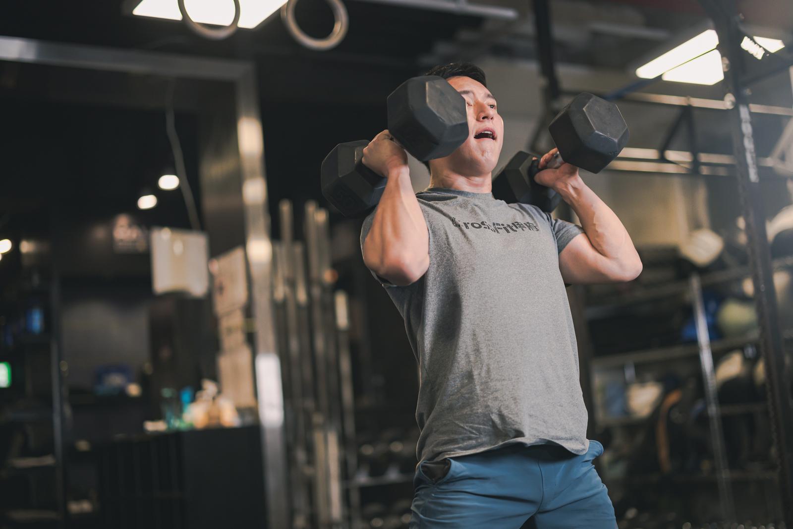 ジムでダンベルを持ち上げてトレーニングする男性［モデル：鈴木秀］