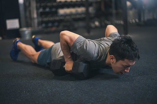 ダンベルを持ってうつ伏せの状態から腕立て伏せの姿勢になる男性（デビルプレス）