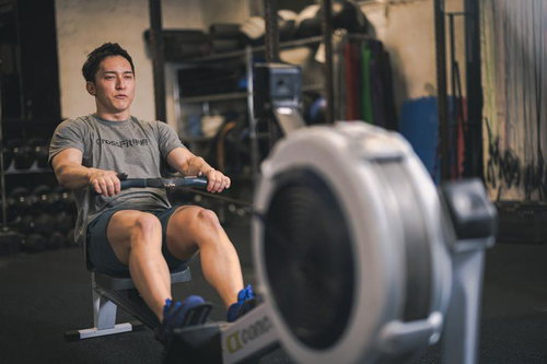 ローイングマシンで筋トレする男性のジムでのトレーニング風景