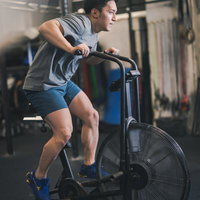 ジムで全力でクロストレーナーを漕ぐ男性の有酸素運動トレーニングの写真