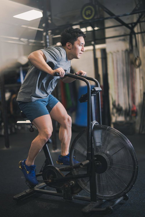 ジムで全力でクロストレーナーを漕ぐ男性の有酸素運動トレーニング