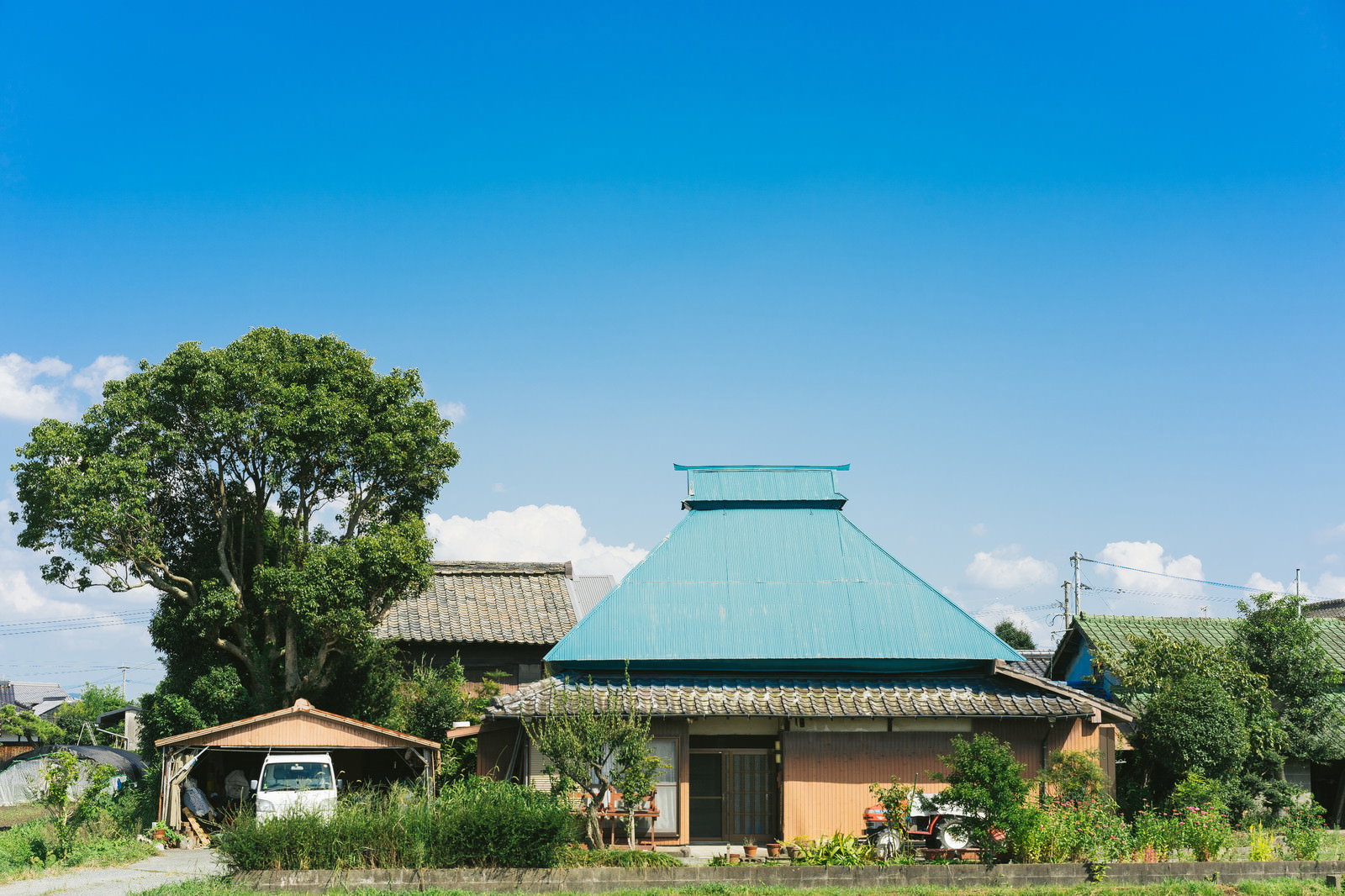 青空の下、緑豊かな自然に囲まれた緑色の屋根を持つ古民家
