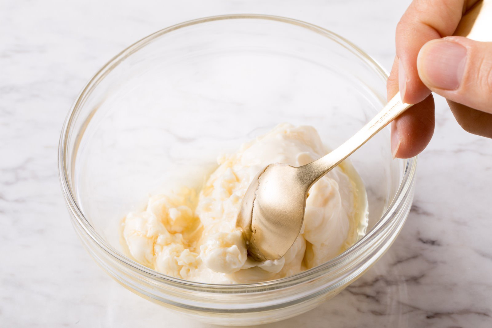 透明なボウルの中でスプーンを使ってはちみつとクリームチーズを混ぜている手元