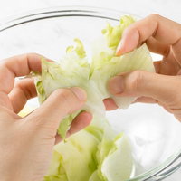 透明なボールに入れたレタスを両手で千切るの写真