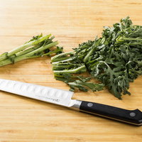 まな板の上で春菊をざく切りする包丁と新鮮な葉物野菜の写真