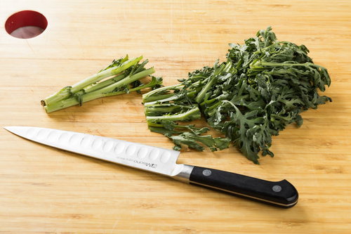 まな板の上で春菊をざく切りする包丁と新鮮な葉物野菜