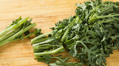 木製のまな板の上で春菊をカットする調理風景