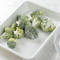 白い容器のブロッコリーに米粉をまぶす調理風景の写真