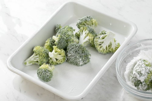 白い容器のブロッコリーに米粉をまぶす調理風景