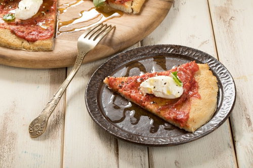 木製テーブルの皿に盛られたクリームチーズを乗せたカリフラワーピザ