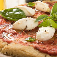 木製まな板に盛られたトマトソースのカリフラワーピザの写真