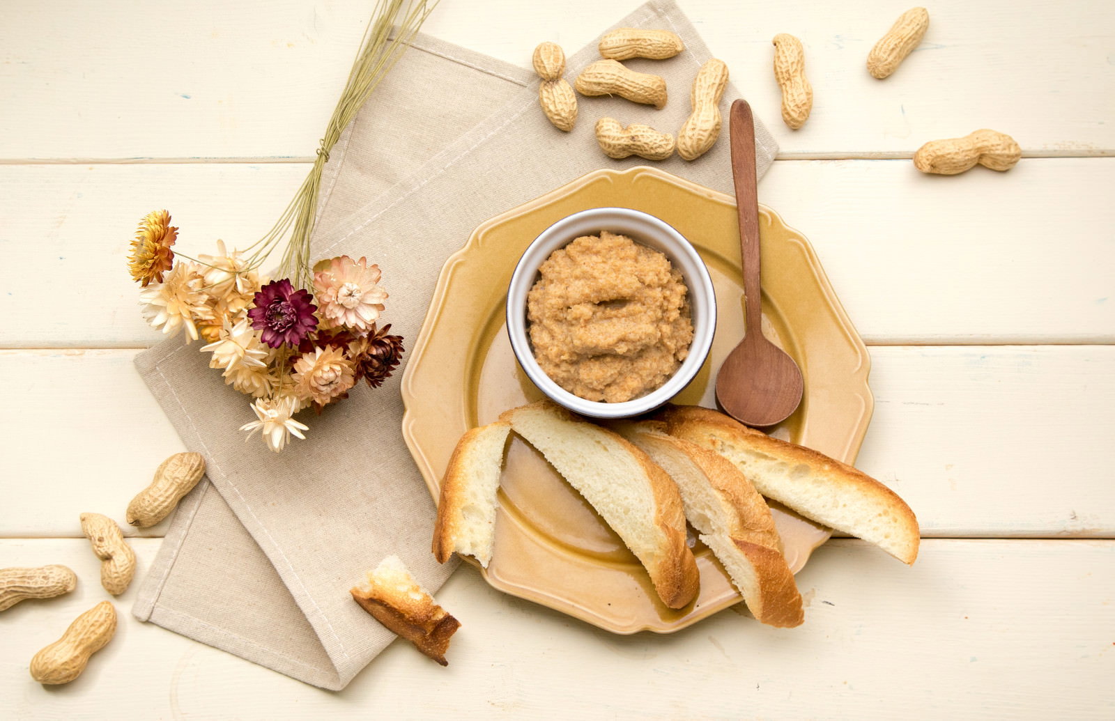 木製テーブルに置かれたピーナッツバターとパン、散らばったピーナッツ