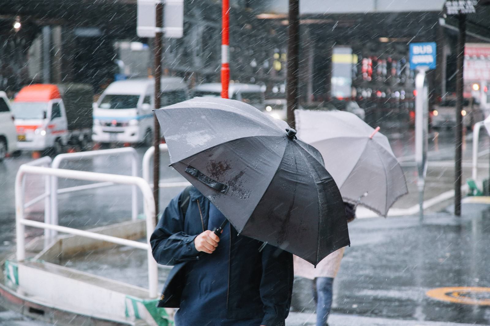 台風の大雨の中を黒い傘で歩く人