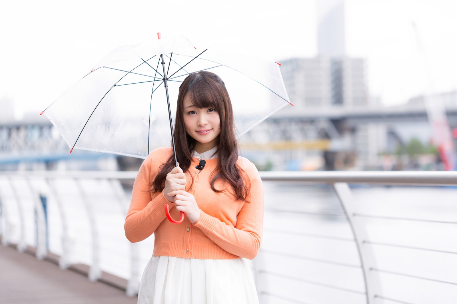 傘とマイクを持って気象予報を伝える女性［モデル：茜さや］