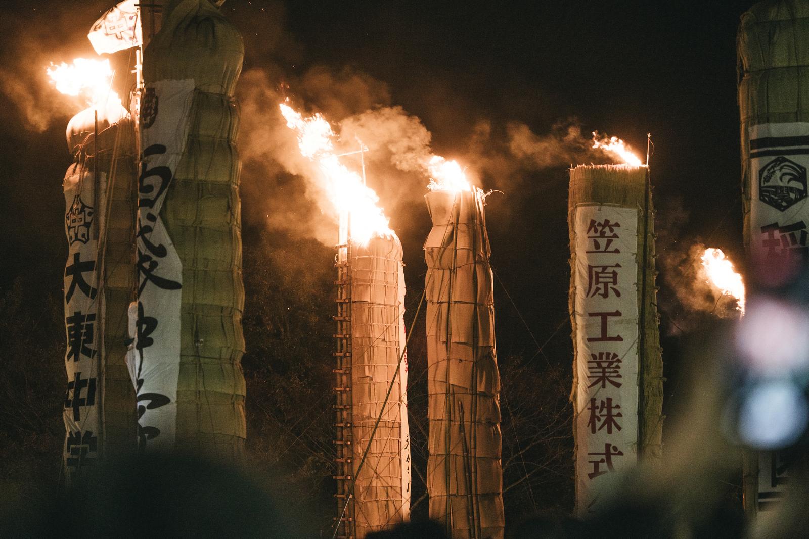 須賀川の松明あかしで夜間に燃え盛る巨大な火柱と、両脇に立つ日本語が書かれた提灯