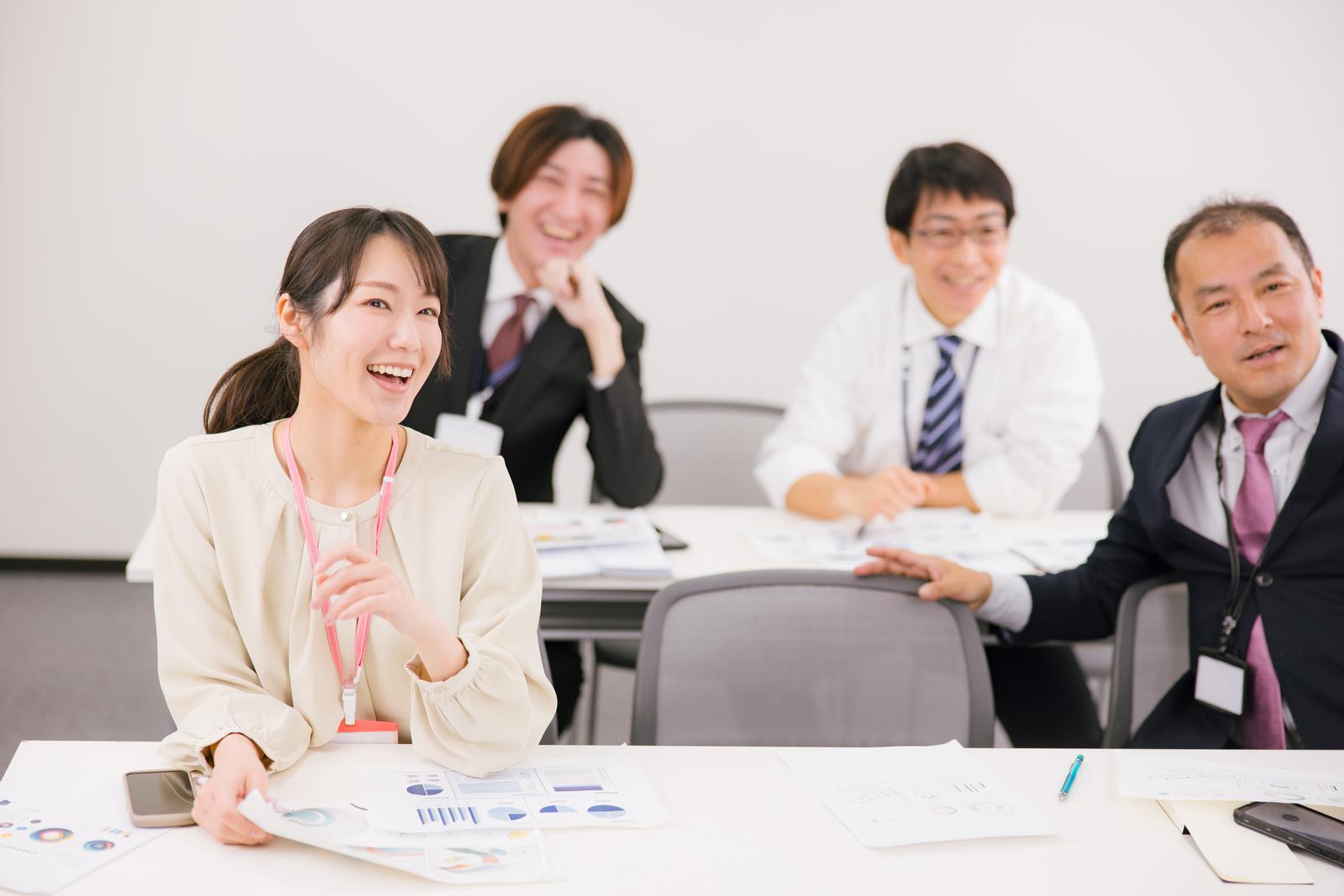 職場の会議室で資料を持ってミーティングをする笑顔の女性ビジネスパーソンと同僚たち［モデル：SAKI 高木桂一］