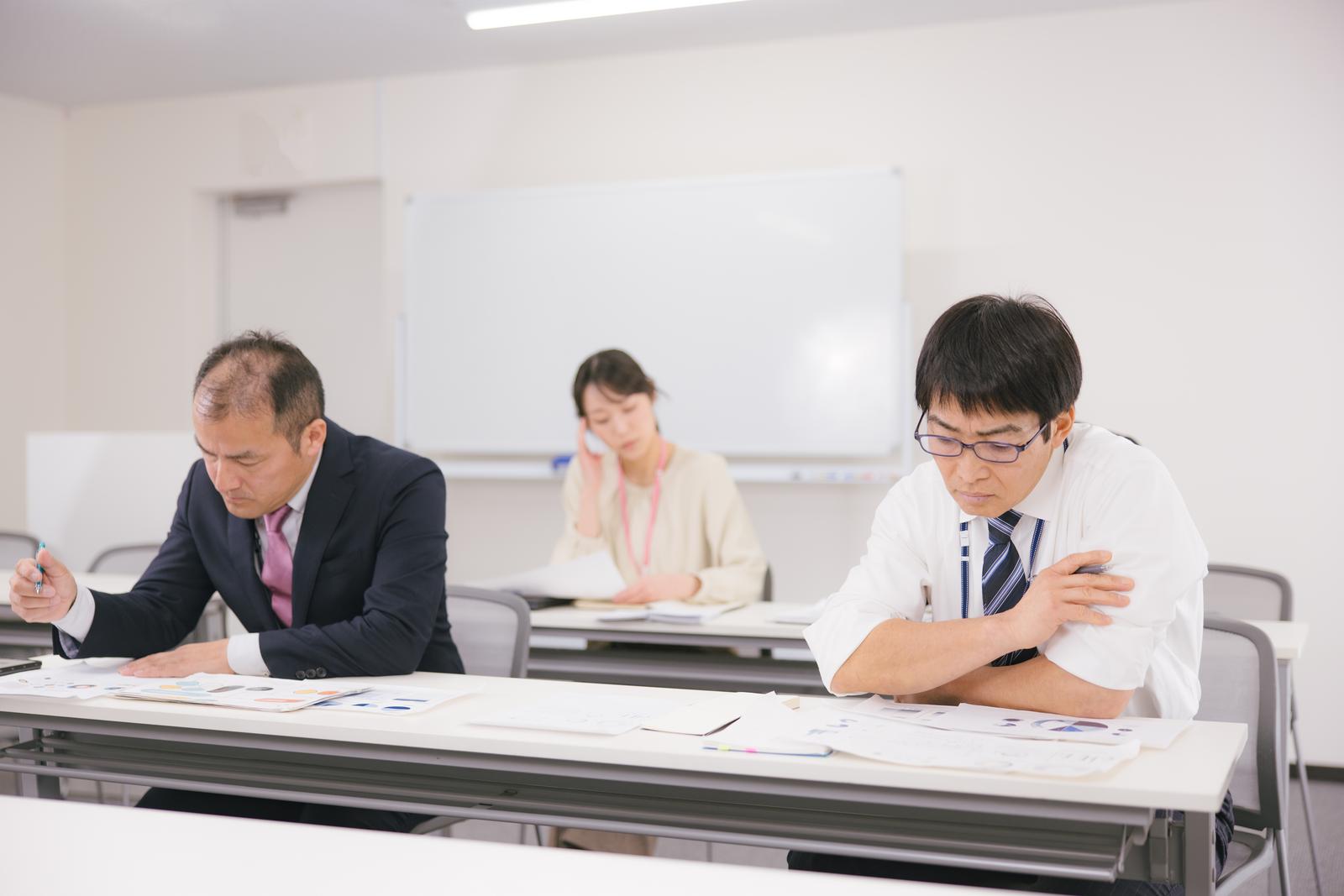 会議室で書類を確認する紺色スーツの男性と眼鏡の男性社員［モデル：ガーミー 高木桂一］