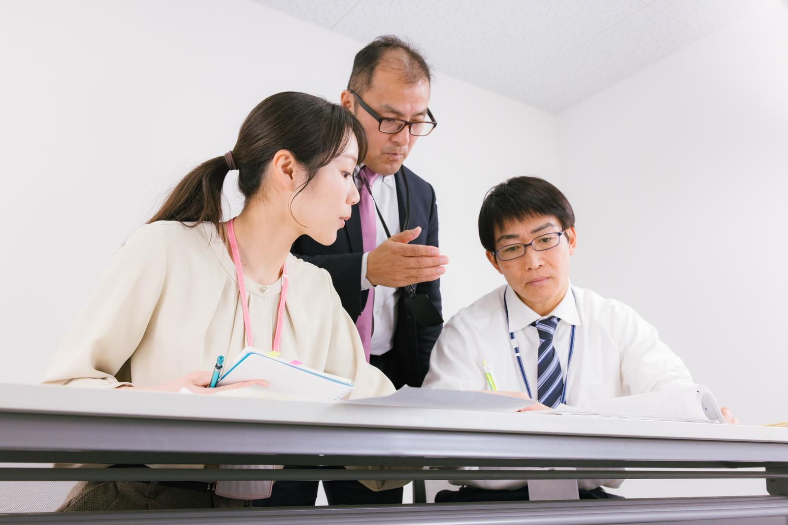 資料を見ながら打ち合わせする男性2人と女性1人の会社員［モデル：高木桂一 ガーミー SAKI］