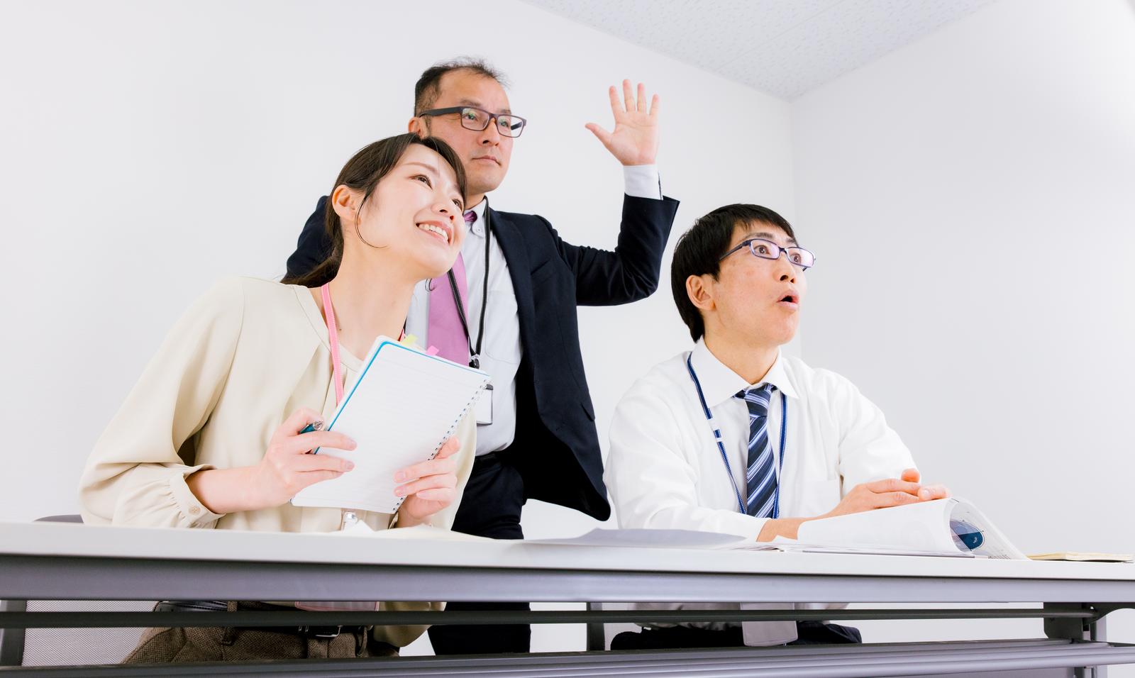 会議中に挙手する男性社員と書類を持つ女性社員［モデル：高木桂一 SAKI ガーミー］