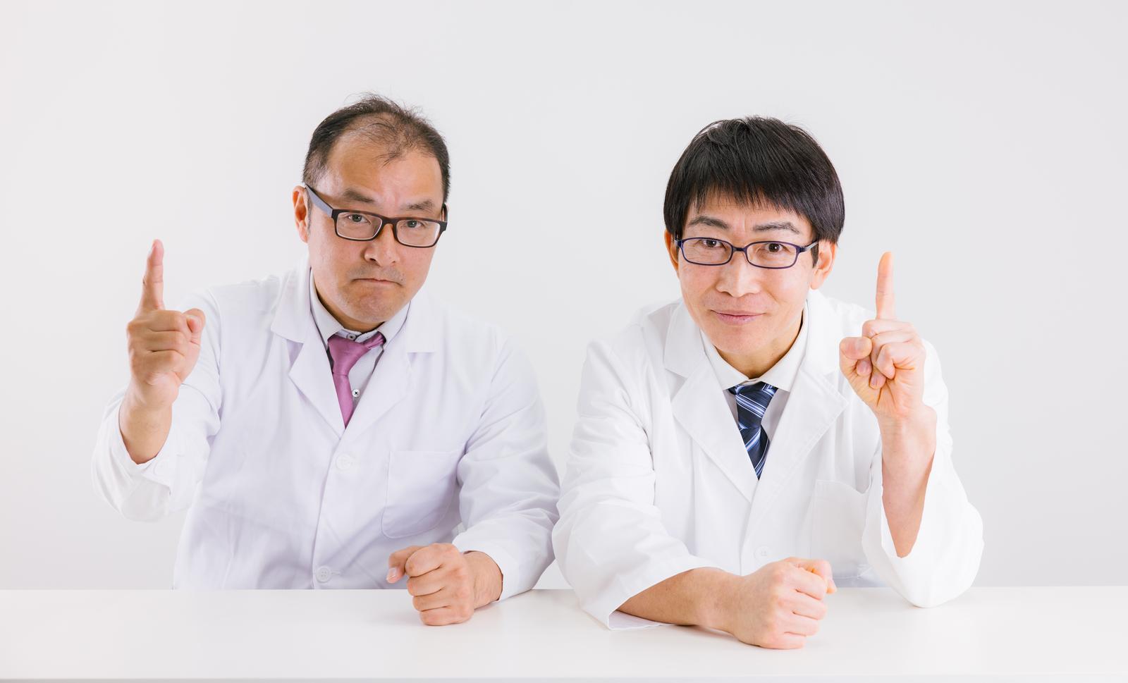 白衣姿の2人の男性医師が人差し指を立てる。研究の成功を示すポーズ［モデル：高木桂一 ガーミー］