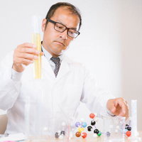 試験管を観察する白衣着用の男性研究員、化学実験室での研究風景の写真