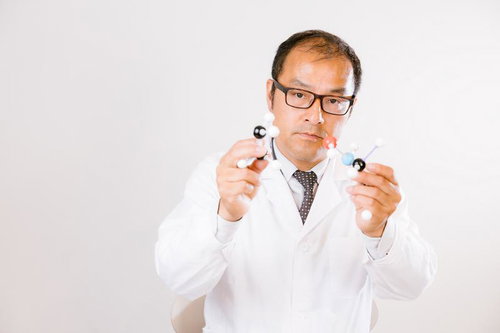 分子構造のモデルを手に持つ眼鏡をかけた白衣の科学者